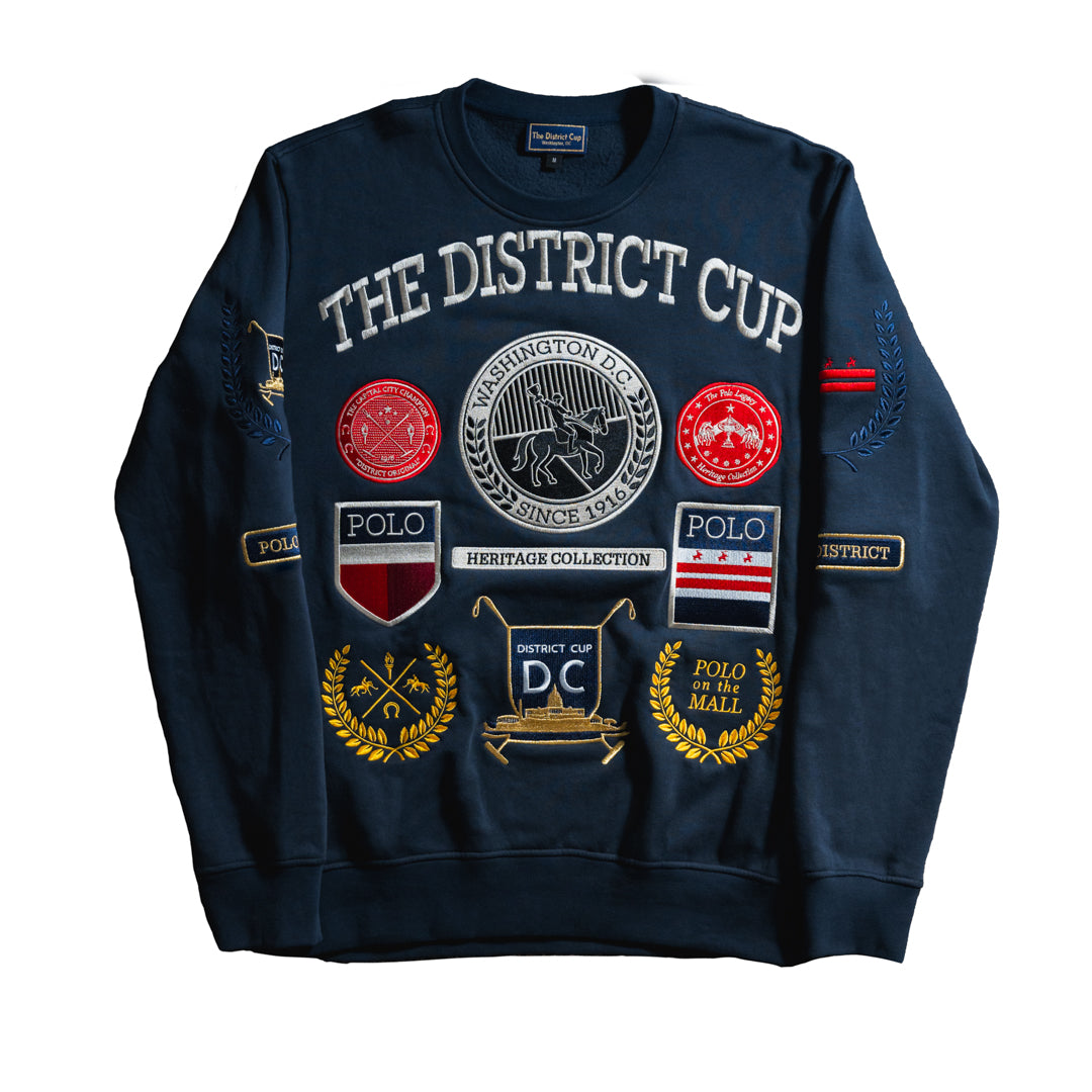 Navy crew neck sweatshirt from The District Cup Heritage Collection featuring embroidered District Cup iconography, Washington D.C. emblems, and ‘Polo on the Mall’ event patches.